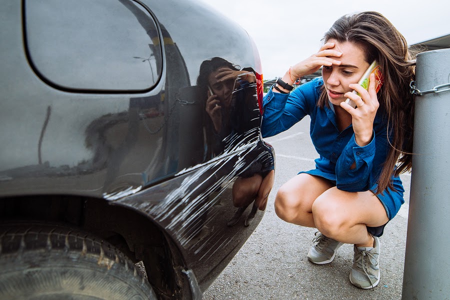 lady on phone looking at paint scratches on her car